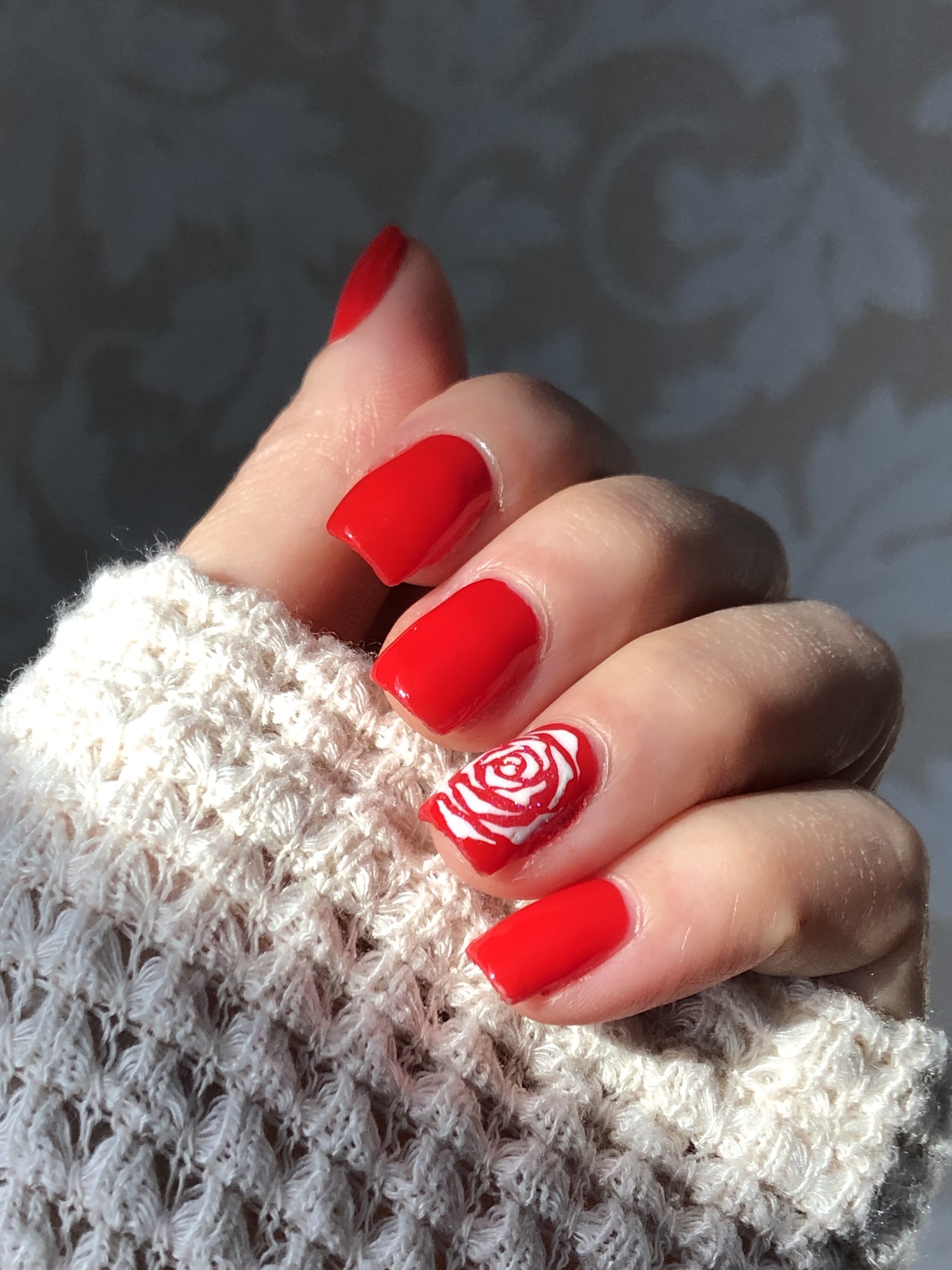 Rode nagels met een wit roosje op de ringvinger
