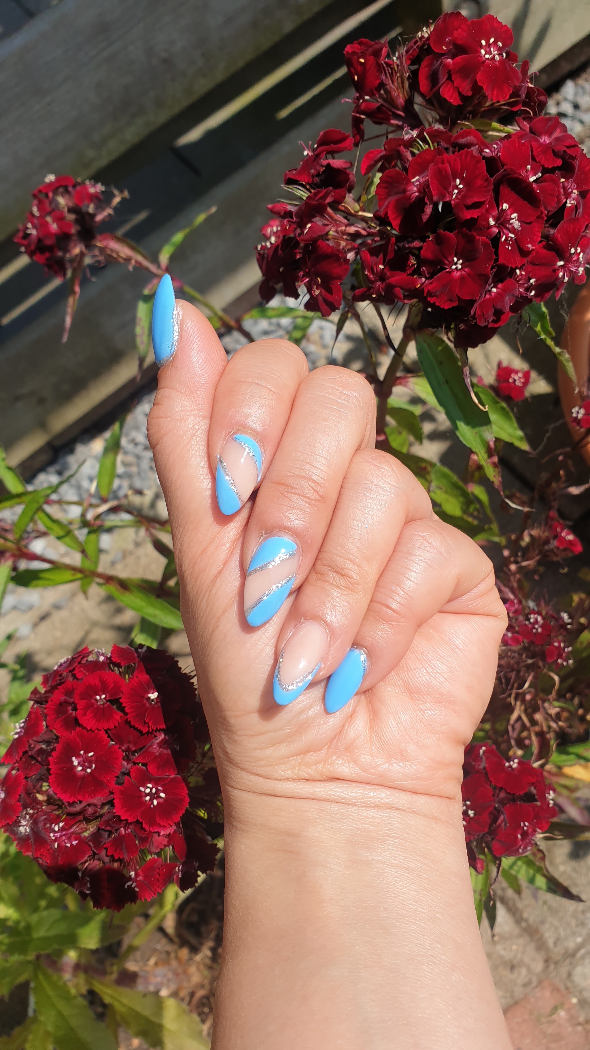 Lichtblauwe nailart, buiten tussen rode bloemen
