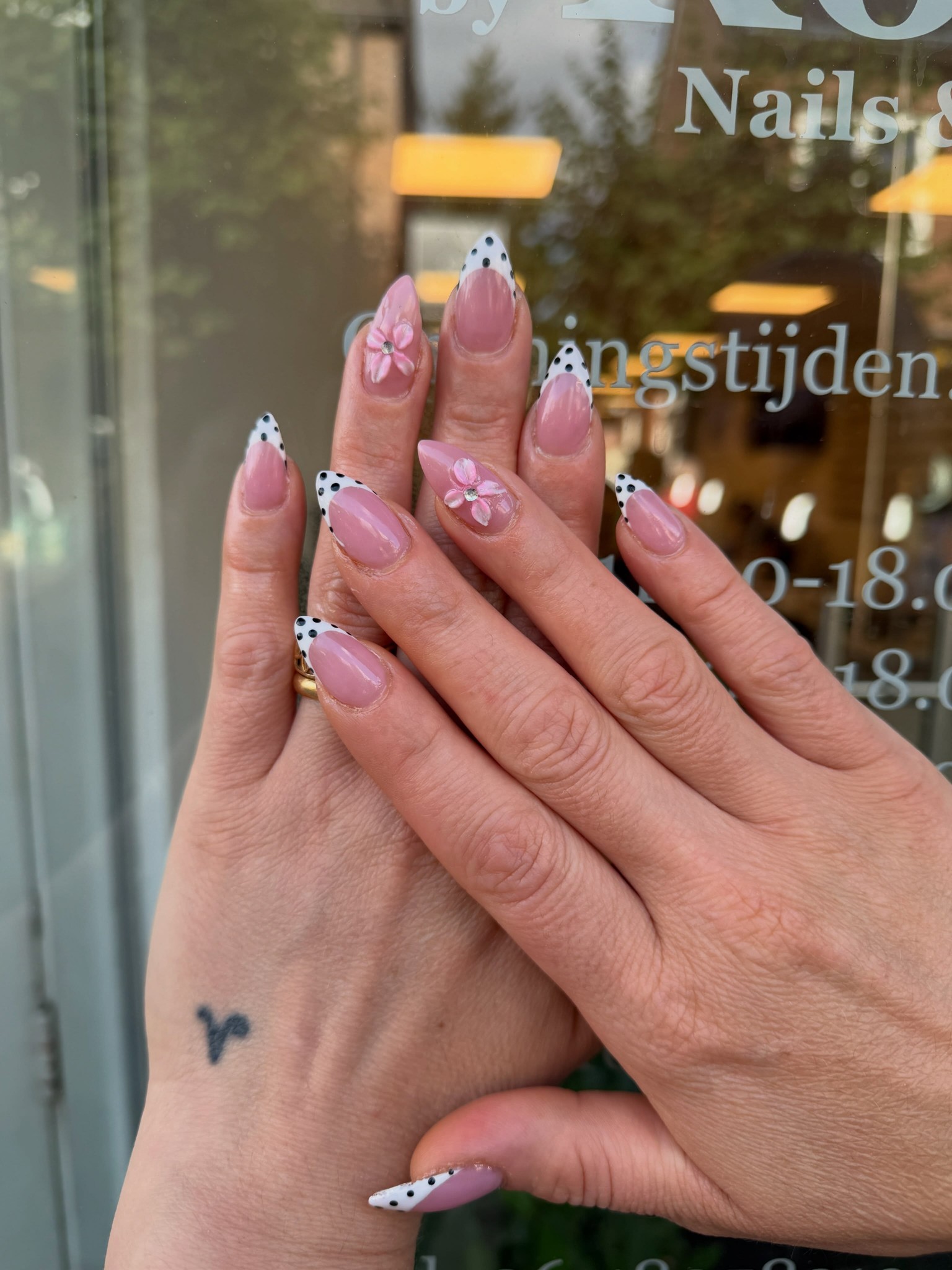 Twee handen met wit-roze stippen nailart voor het raam van de salon